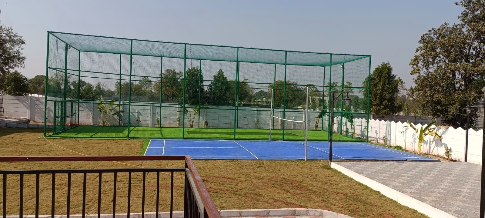 The netted box cricket enclosure and the blue multi-sport court used for badminton and pickleball.